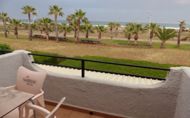 Balcón blanco con mesa y sillas con vistas al mar y el paseo marítimo