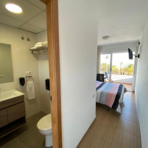 Vista del interior de una de las habitaciones con el baño en primer plano, la cama con televisor y puerta de terraza al fondo