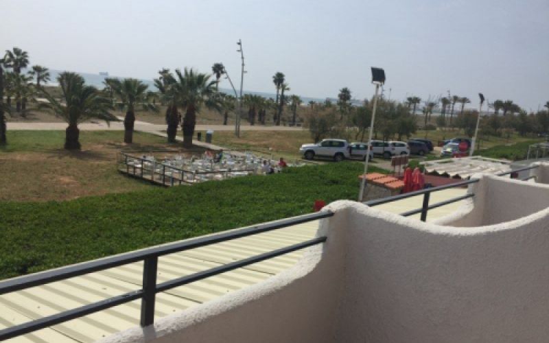 Vista del mar al fondo y el paseo marítimo con palmeras desde el balcón de una habitación en zona superior